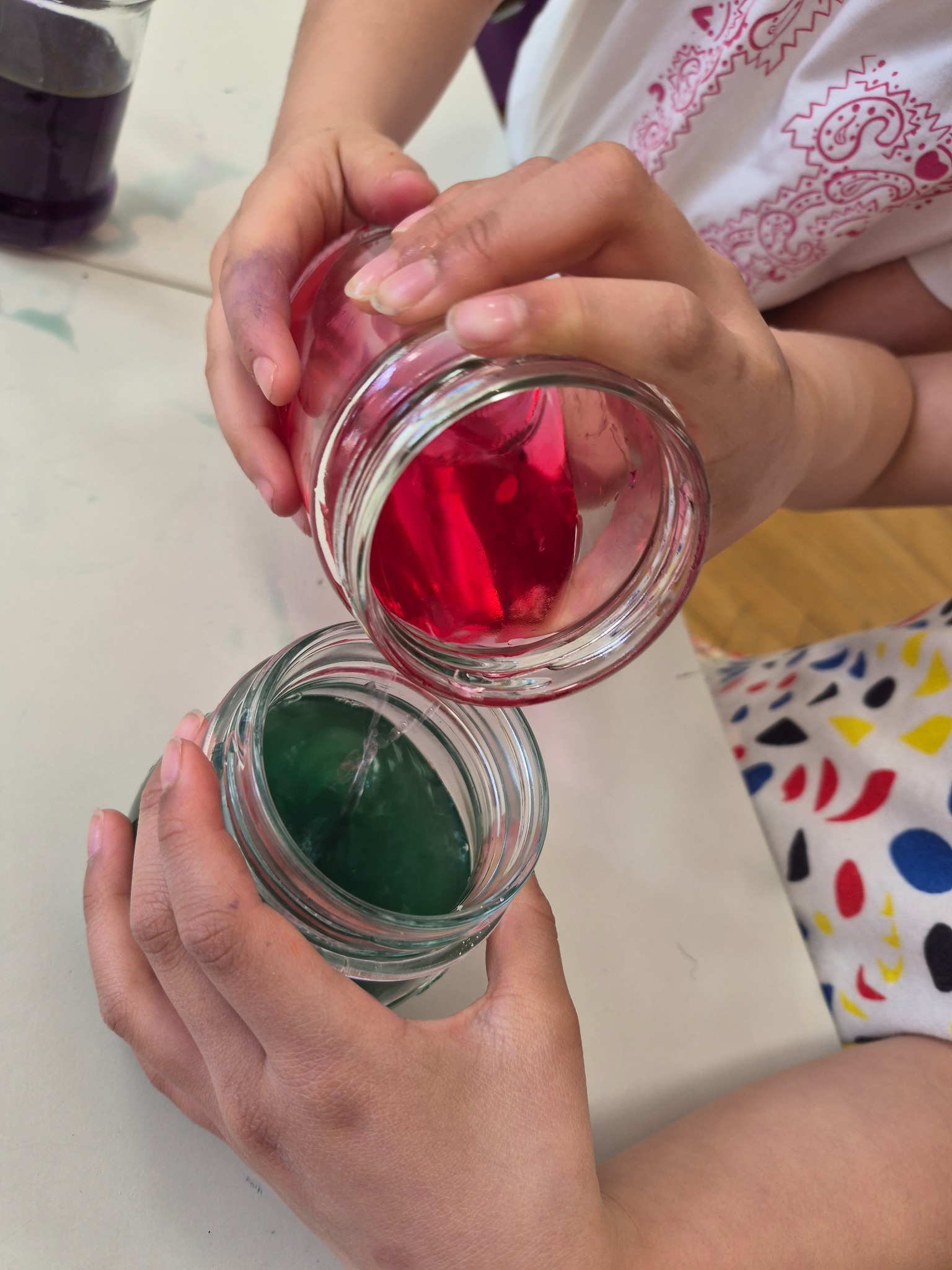 Child pouring red colour into green botanical liquid